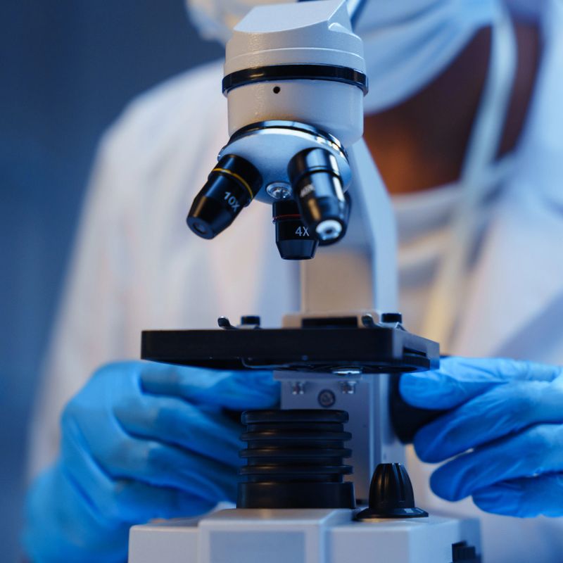 A close-up of a microscope and a scientist's hands in protective gloves on a blue background