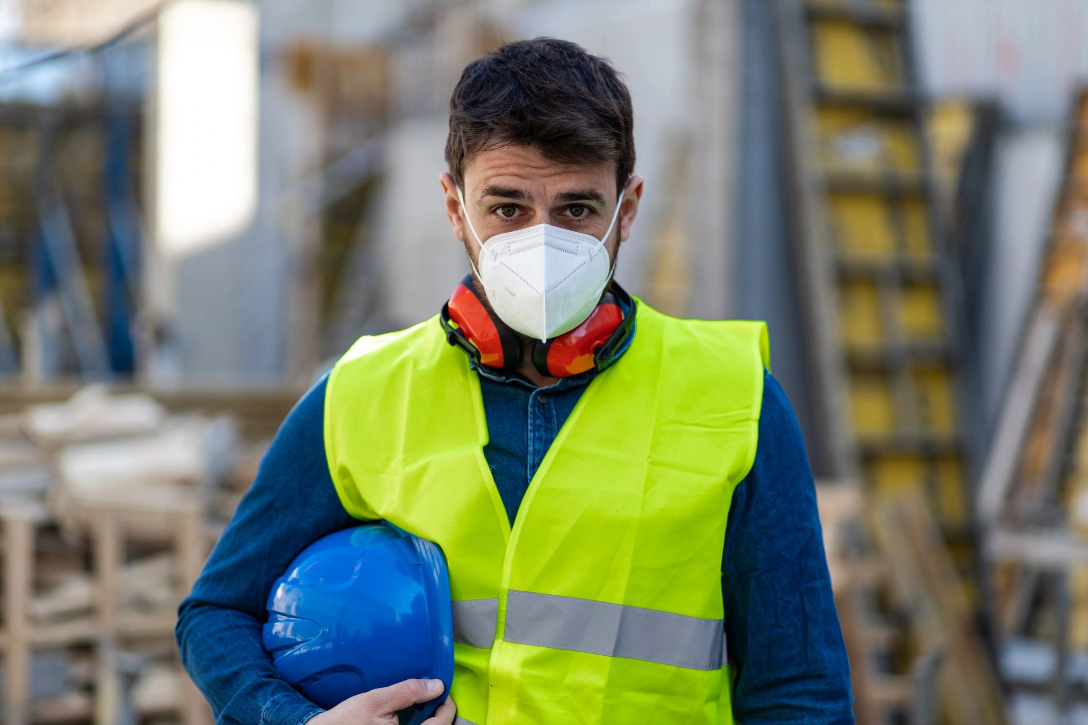 Worker in a safety vest and disposable respirator, holding a hard hat