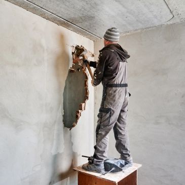 Construction worker demolishing a wall inside a building.