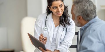 A female doctor consulting an elderly male patient with a tablet.