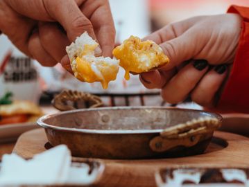 Two hands dipping bread into melted cheese in a rustic pan.