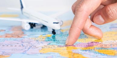 Hand pointing to a destination on a colorful world map beside a model airplane.