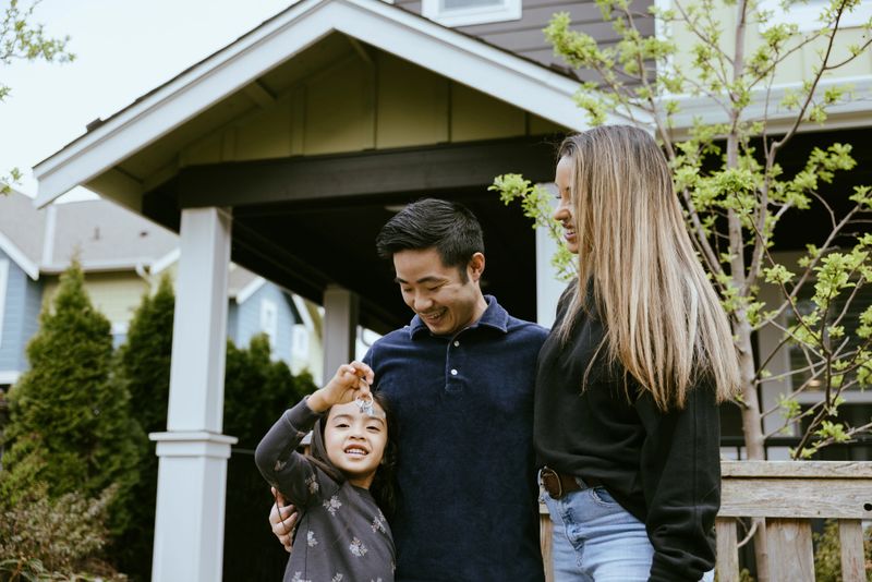 A mixed race husband, wife, and their daughter hold up the keys to their new house, smiling with joy and excitement at their investment.