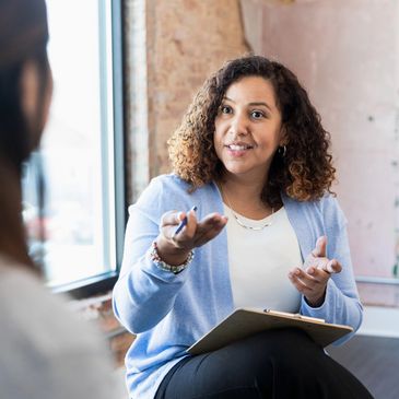 A woman in a blue cardigan listens and gestures while talking to another person.