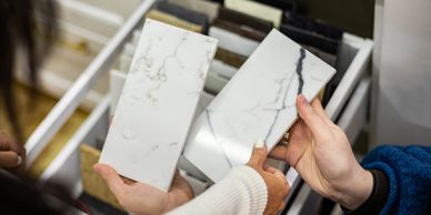 Two people comparing marble tile samples indoors.