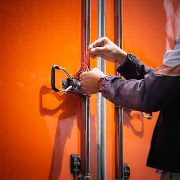 Person locking an orange container door with a padlock.