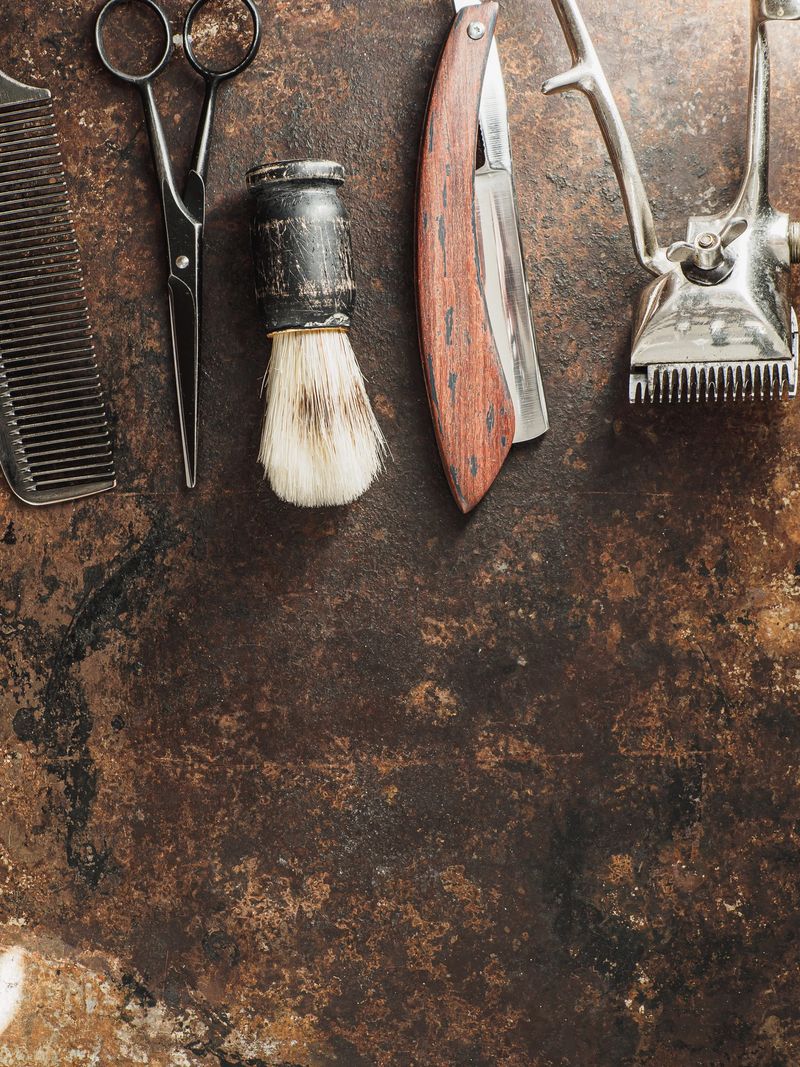 vintage barber tools: dangerous razor, hairdressing scissors, old manual clipper, comb, shaving brush on rusty background. top view flat lay. copy space. Vertical orientation.