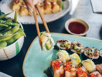 Chopsticks holding sushi with edamame and sauce on the side.
