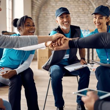 A group of diverse volunteers joining hands in a team cheer.