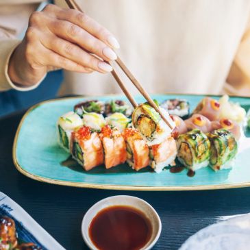 Person picking sushi with chopsticks from a blue plate.