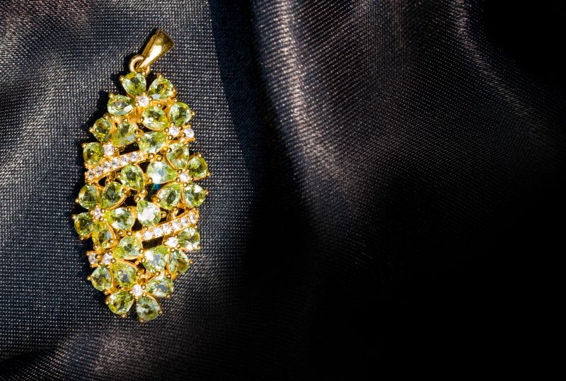 Peridot and Diamond Jewel or gems pendant on black shiny polyester fabric background. Collection of natural gemstones accessories. Studio shot