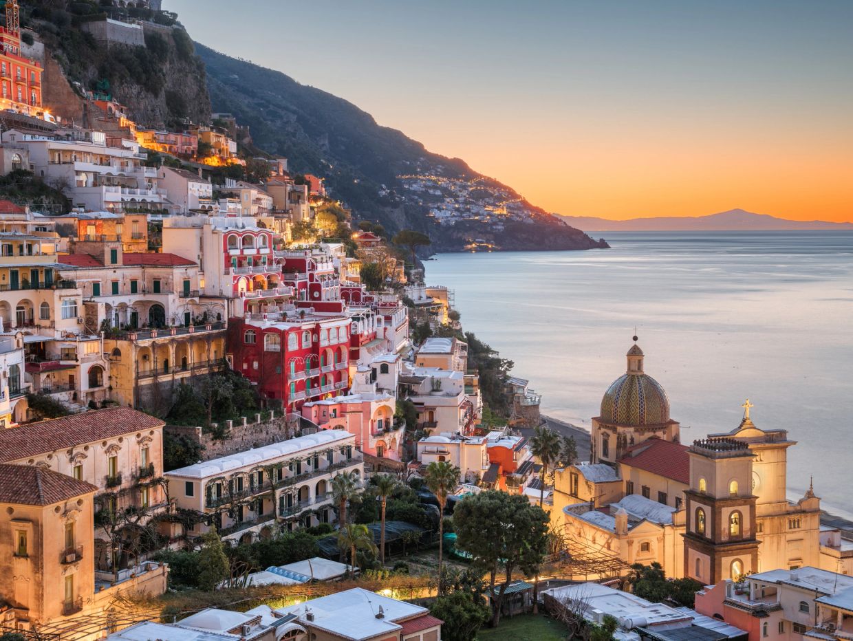 Sunset view of a coastal town with colorful buildings and a church dome.
