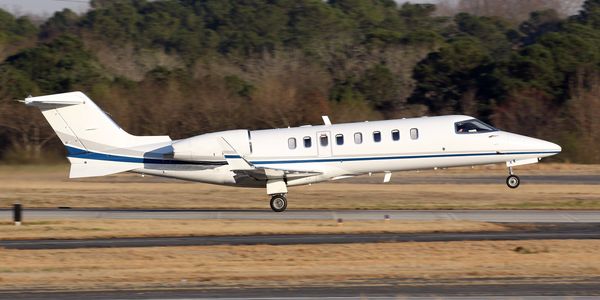 White private jet landing on a runway with trees in the background.