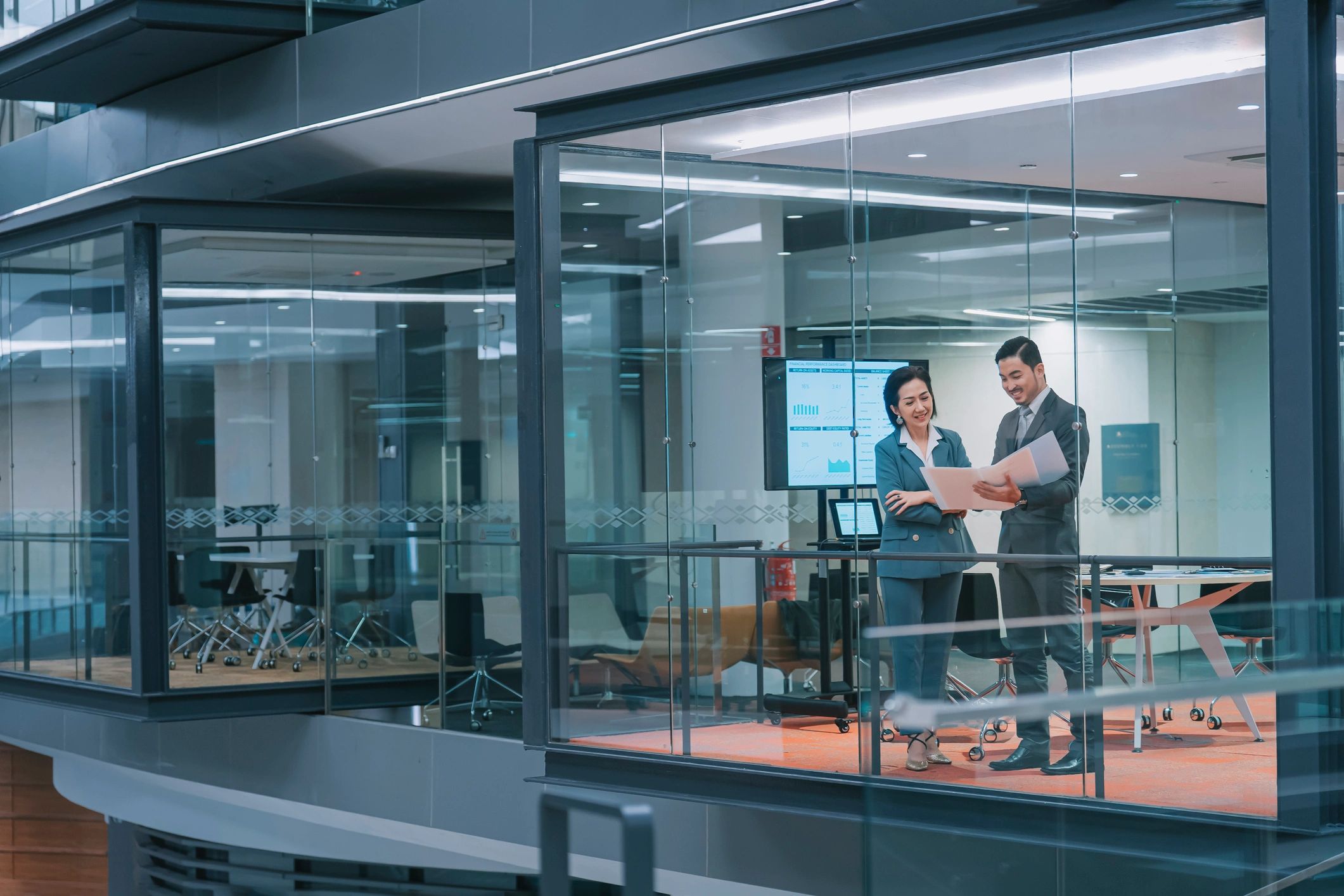 Two business professionals discussing documents in a modern glass office.