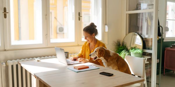 Woman working on laptop with her dog beside her.
