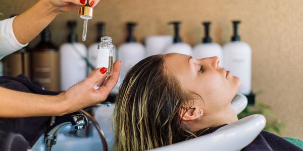 Person getting hair treatment with a serum at a salon.