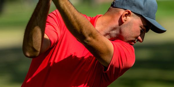 Man in red shirt and blue cap preparing to swing golf club.