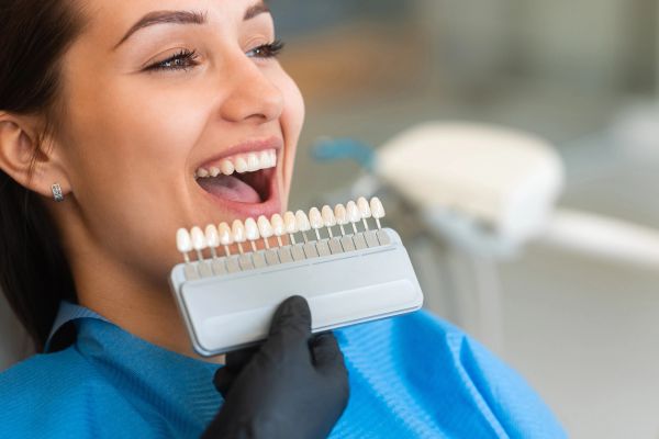 Woman smiling with dental shade guide near her teeth.