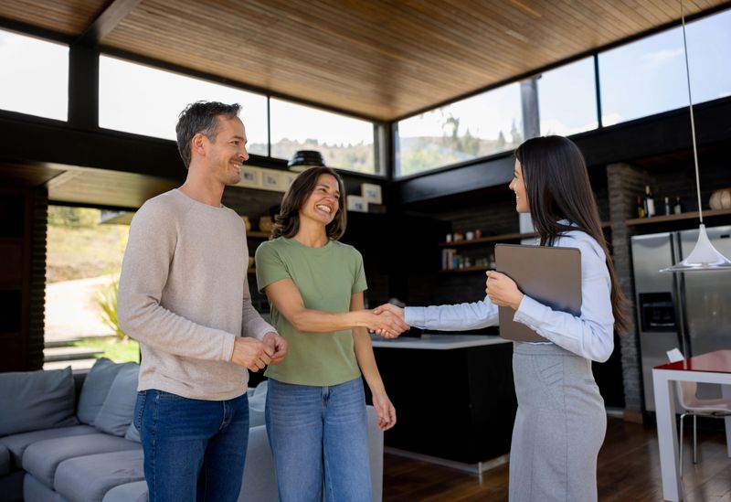 Happy real estate agent handshaking with a couple of customers interested in buying a house - home ownership concepts
