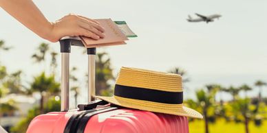 Hand holding passport and boarding pass over a suitcase with plane flying in background.