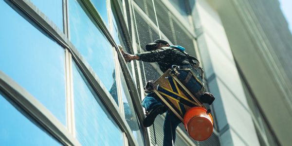 A worker cleaning tall building windows suspended by ropes.