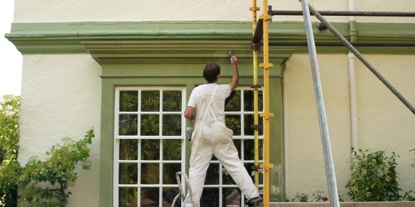 Painter working on house exterior near scaffolding.