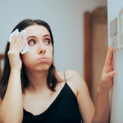 Woman wiping sweat and looking at thermostat.