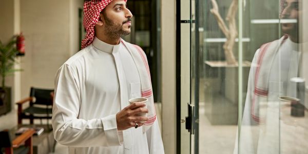 Un homme en tenue traditionnelle regarde par une fenêtre.