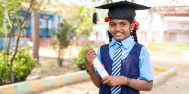 Smiling young girl in graduation cap holding diploma outdoors.