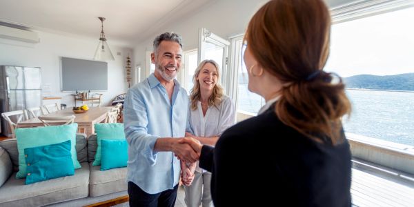Couple shaking hands with a woman in a bright living room.