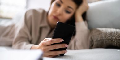 A woman lying on a couch looking at her phone with a tired expression.
