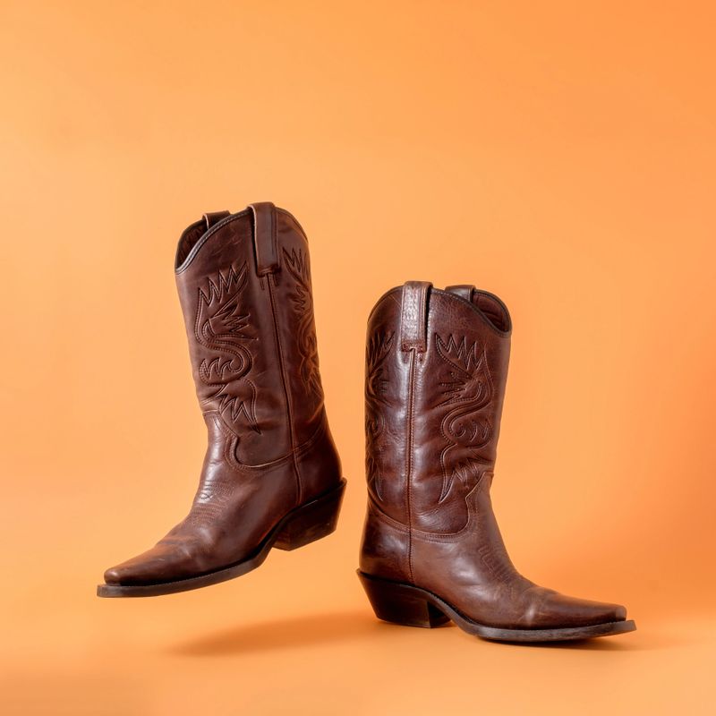 Two elegant classic cowboy boots on an orange clay background. Ranger cowboy concept on a ranch in america usa texas.