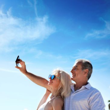 Couple enjoying a sunny day, taking a selfie with a bright blue sky.