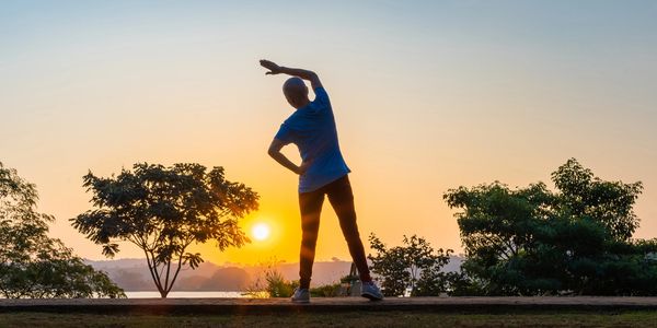 Person stretching outdoors during sunrise with scenic trees.