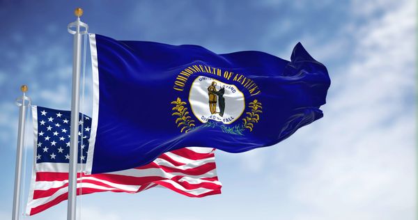 Kentucky and USA flags waving against blue sky.