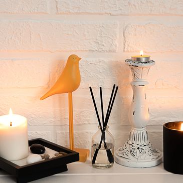 A cozy arrangement of candles, a bird figurine, and reed diffuser on a white surface.