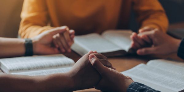 People holding hands and reading the Bible.