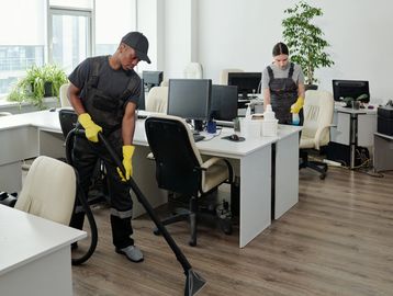 Two janitors cleaning an office with vacuum and spray bottle.