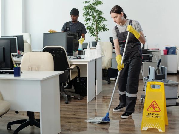 Two janitors cleaning an office with a caution wet floor sign.