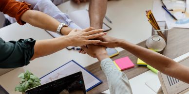 Team joining hands in a collaborative office setting.