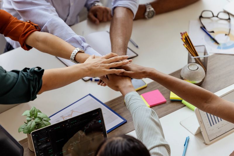 Multiracial business team putting hands together, showing support and unity after a successful presentation at company meeting