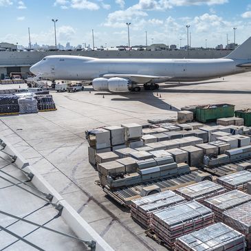 Large cargo airplane parked with shipping containers and trucks nearby.