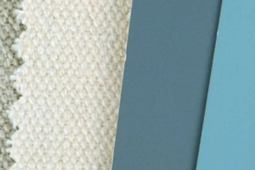 Fabric swatches and paint sample cards in various shades of blue and beige on wood.