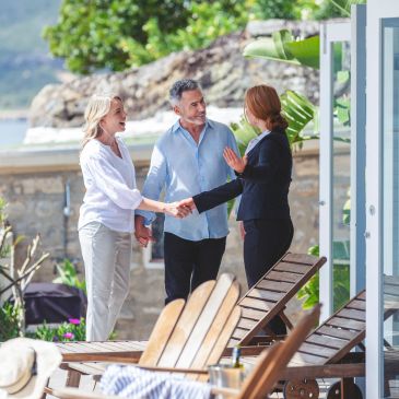 Couple greeting a real estate agent outdoors near a pool.