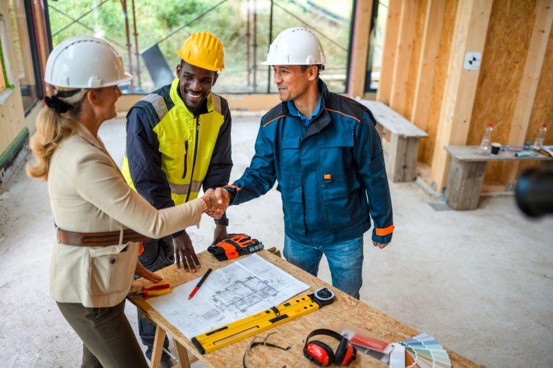 Serious businesswoman and contractor closing a deal for the development of a new residential housing project. They are shaking hands in front of a colleague.