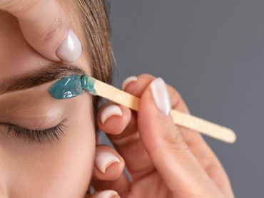Applying blue wax to shape eyebrows with a wooden spatula.