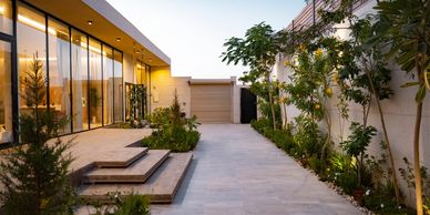Modern house exterior with large glass windows and landscaped garden at dusk.