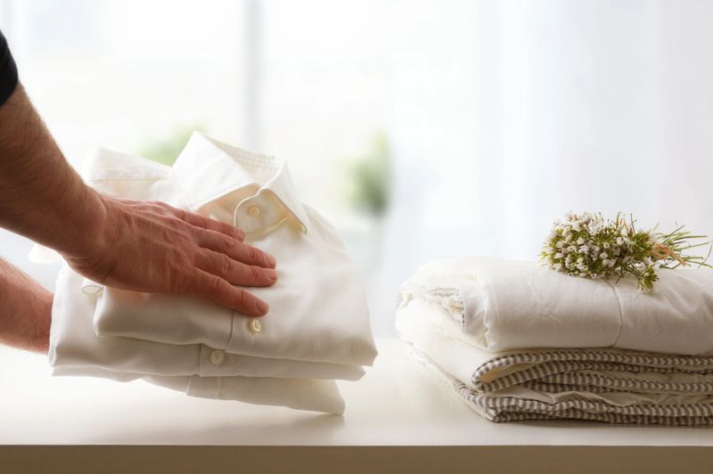 Man leaving freshly washed and ironed clean shirts on white table and window background in a room. Front view. Horizontal composition.