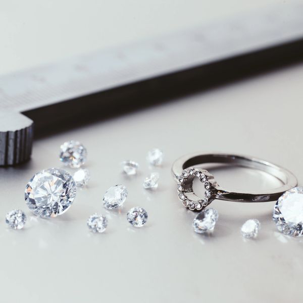 Loose diamonds and a ring next to a caliper on a white surface.
