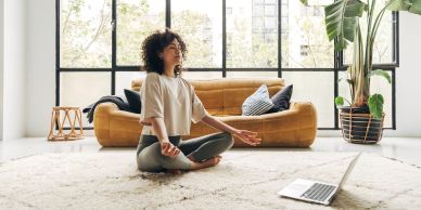 Mujer meditando frente a una laptop en la sala.